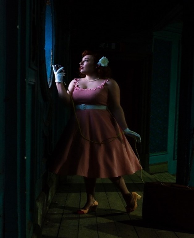 Women dressed up in vintage clothes stood in a dark room and looking out of the window